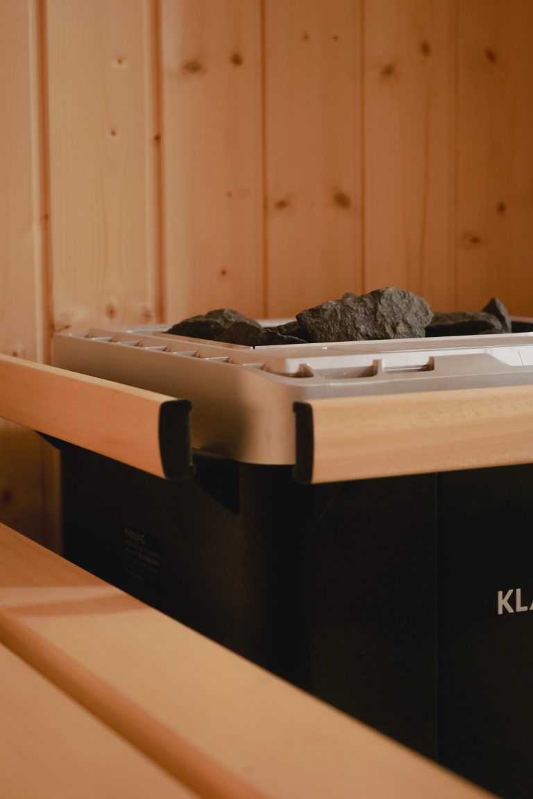 Ofen in einer Sauna vor einer Holzvertäfelten Wand.
