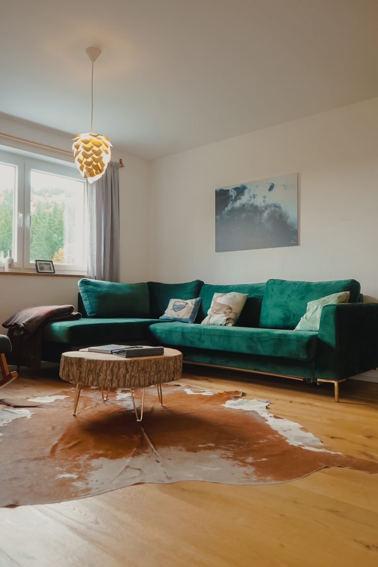 Eine grüne Couch in L Form, davor ein Holztisch und ein Kuhfell-Teppich.