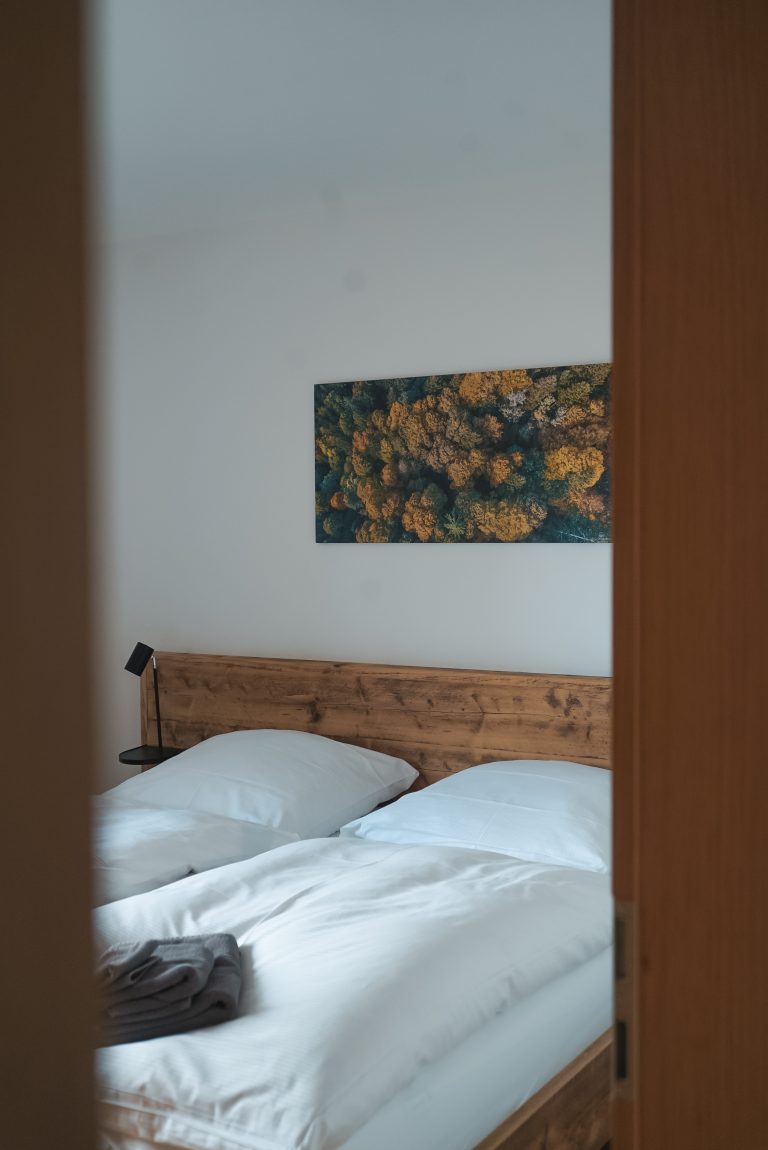 Blick durch Türrahmen in ein geräumiges Schlafzimmer mit einem großen Doppelbett und einem Bild im Hintergrund