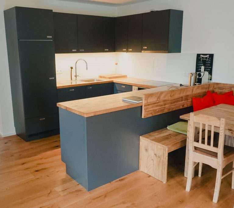 Blick in eine moderne, schwarze Küche mit einem Esstisch und einem Holzboden